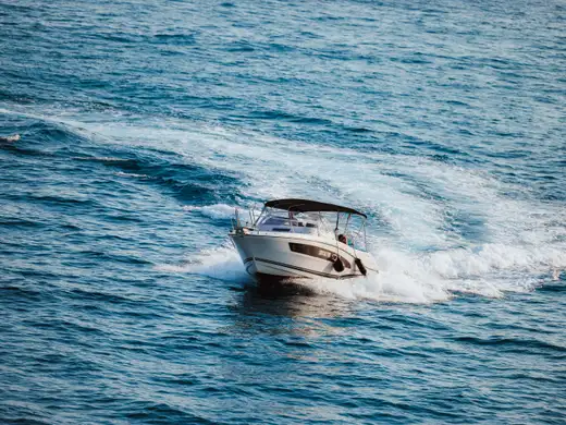 The boat seen from astern, throwing a wide wake across open blue water