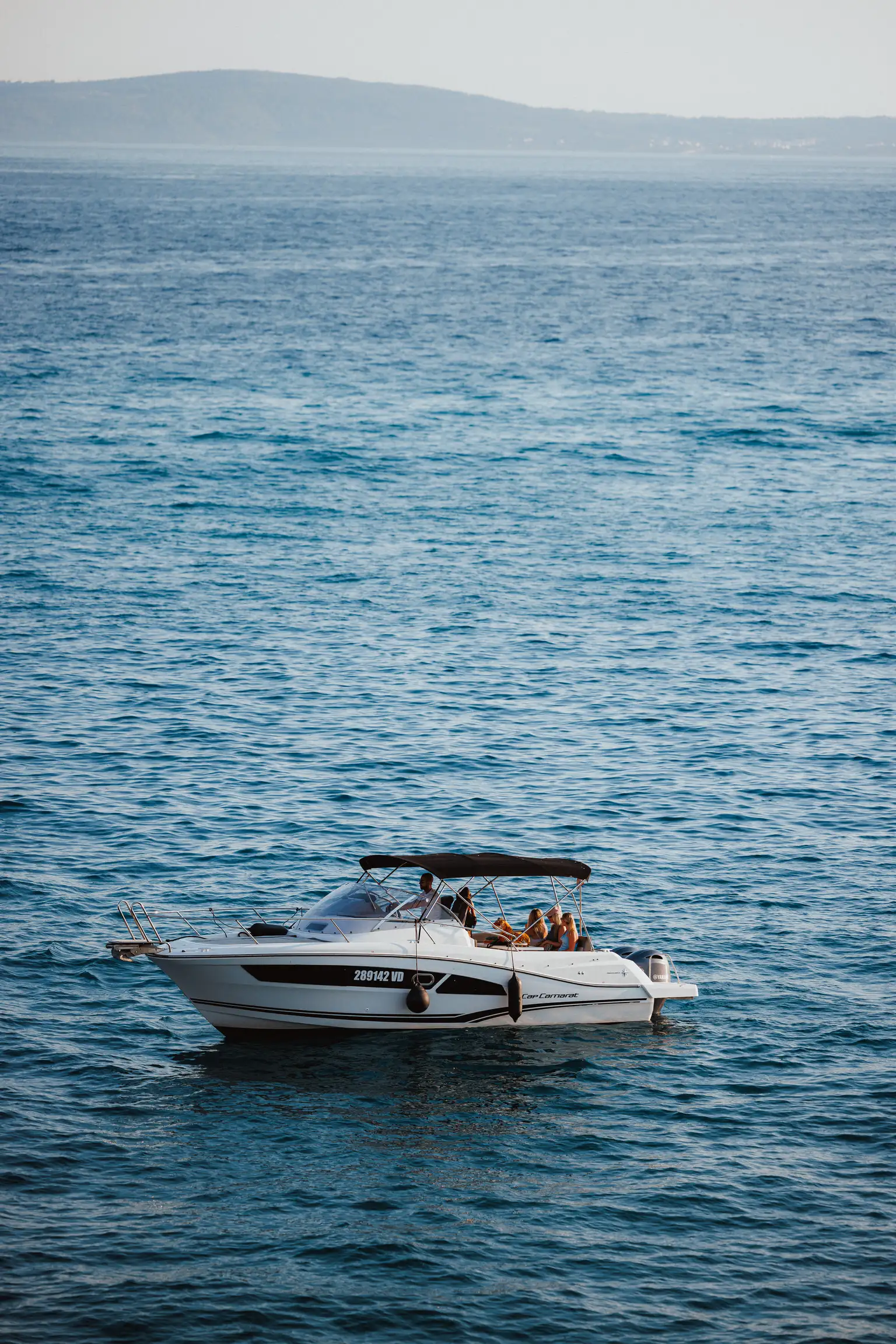 Our white cabin boat out on open blue water, its dark bimini top up over the cockpit