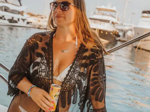 A guest in sunglasses holding a drink aboard the boat in a marina