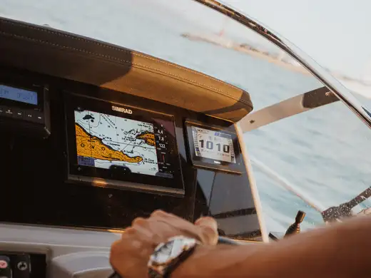 The skipper's hand on the wheel beside the navigation display and dashboard